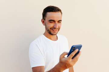 Stylish young man typing smart phone on orange background.