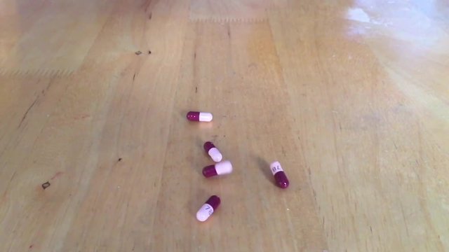 Caplet pills falling in slow motion onto wood table with natural light angling in from background. 