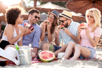 Happy young friends eating watermelon on the beach