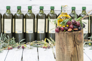 Obraz na płótnie Canvas Una aceitera y aceitunas negras con hojas, botellas de aceite de oliva desenfocadas 
