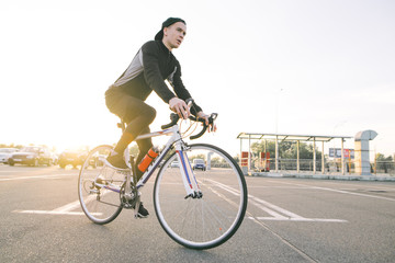 Portrait of an attractive cyclist in motion. Young rider in dark bike wears a bike on a street background and sunshine in the sunset.