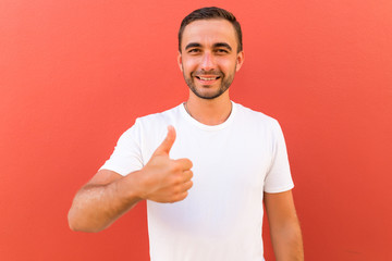 Handsome young man gesturing thumbs-up isolated on red background