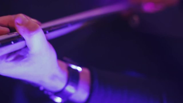 Rock guitarist on a stage in a backlights playing rock music, hand hits the strings, close up view