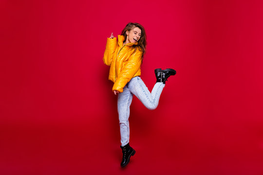 Full-lenght portrait of active happy girl with long hair dressed yellow jacker and jeans with happy smile over red wall. Portrait of a frustrated young woman in dress isolated over red background