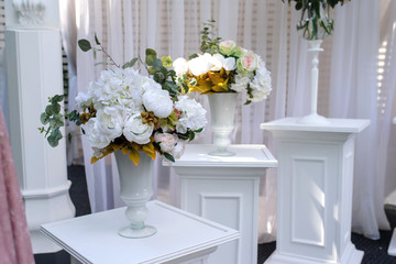 Closeup photo of white pillars with vases with flowers on them and a part of an wedding arch with white curtains on background