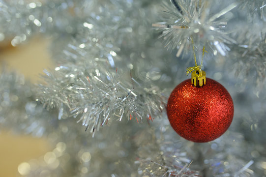Closeup photo of a red Christmas ball hanging on a silver tree