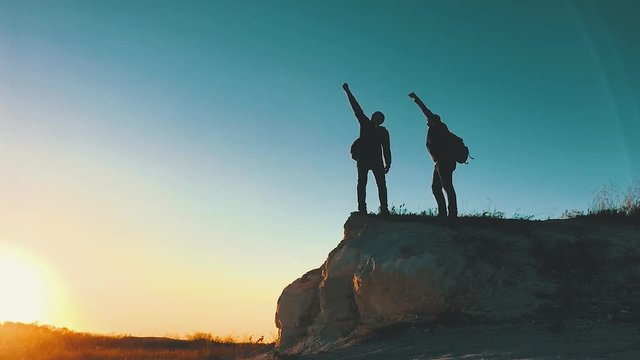 Silhouette of helping hand between two climber. two hikers on top of the mountain, a man helps a man to climb a sheer stone. couple hiking help each other silhouette in mountains with sunlight.