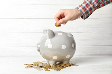 Man putting coin into piggy bank on table