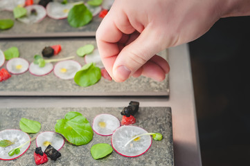 A cook adds a pinch of salt to an artistic plating of micro green and radish salad.