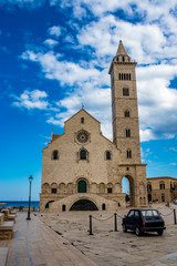 Fototapeta na wymiar The beautiful Romanesque Cathedral Basilica of San Nicola Pellegrino, in Trani. Construction in limestone tuff stone, pink and white. vintage car parked. In Puglia, near Bari, Barletta, Andria, Italy.