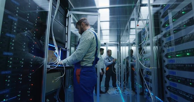 Wide shot of a male technicians working in a data center carrying cable down the corridor amongst rows of server racks