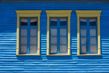 Fachada con tres ventanas con marcos amarillos y muro azul