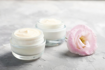 Fototapeta na wymiar Closeup view of hand cream jars with flower on gray background
