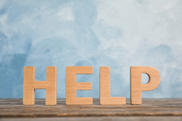 Word "Help" on wooden table against color background