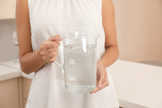 Woman holding glass jug with water in kitchen, closeup