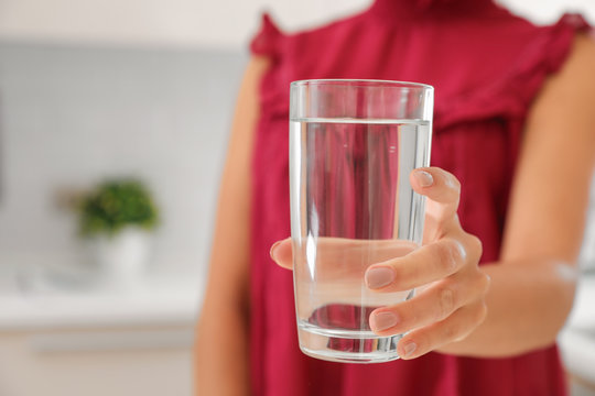 Woman holding glass with water in kitchen, closeup. Space for text