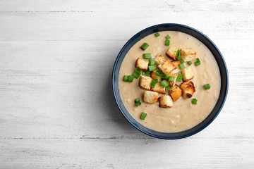 Bowl of fresh homemade mushroom soup on wooden background, top view with space for text
