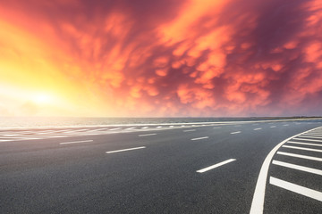 Fototapeta premium Asphalt road and dramatic sky with coastline at sunset