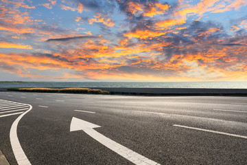 Fototapeta premium Asphalt road and dramatic sky with coastline at sunset
