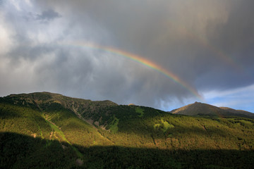 Fototapeta na wymiar Bright Rainbow in the sky above Kanas Nature Reserve. Xinjiang Province, China. Clouds, alpine high altitude forest and fresh air. Altai Mountains near the border of, Kazakhstan, Russia and Mongolia.