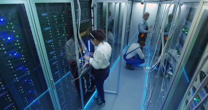 Medium timelapse shot of people working in a data center with rows of server racks checking the equipment and discussing their work
