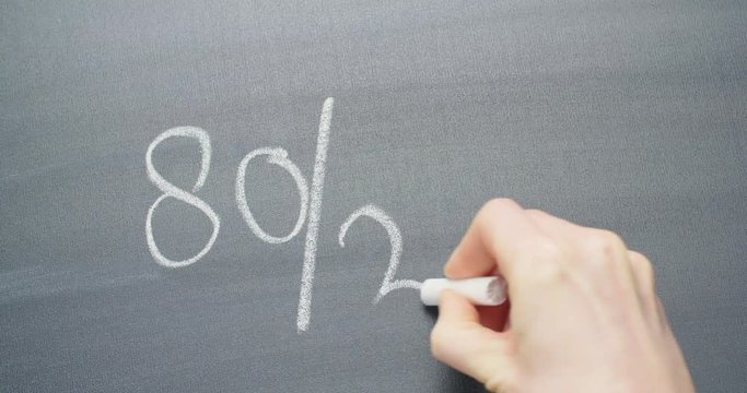 Hand writing out the Pareto principle - 80/20 with chalk on a blackboard.