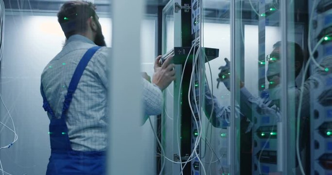 Medium shot of two people working in a data center install server hardware into a rack