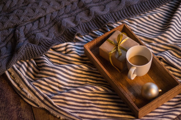 Winter decor: cup of coffee, a gift, a tray, a ball and a cozy striped plaid