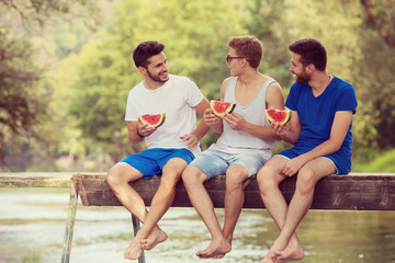 men enjoying watermelon while sitting on the wooden bridge