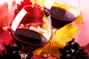Semi-sweet red wine in large glasses, autumn still life with red and yellow leaves on pink...