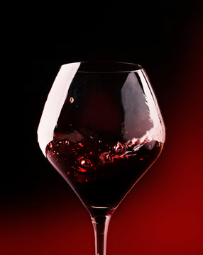 Red wine, splash in a glass, dry cabernet sauvignon, dark red background, defocused in motion image, shallow depth of field