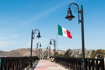 Pedestrian bridge leading to the marina and waterfront shops in Ensenada, Mexico, with a giant flag...