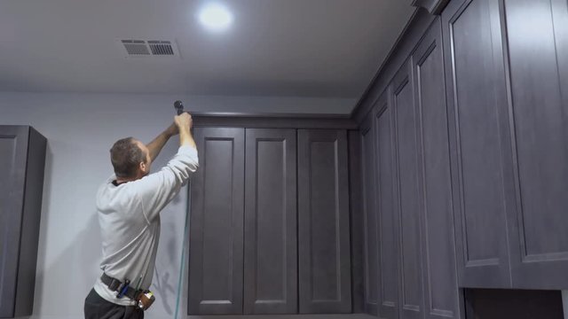 Handyman working using brad nail air gun to Crown Moulding on kitchen wall cabinets framing trim, with the all power tools