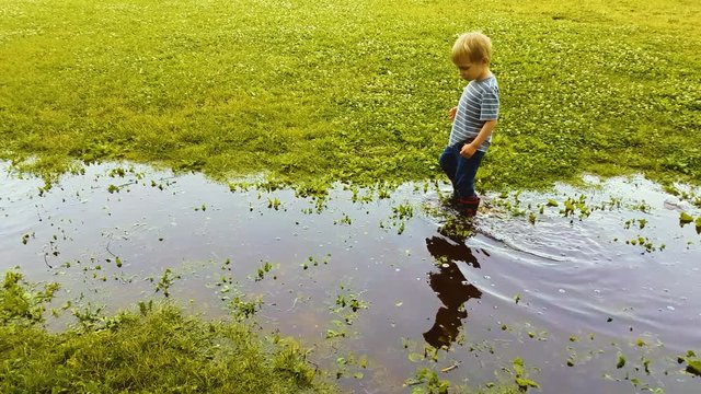 Two preschoolers explore and wade through a giant puddle in a field