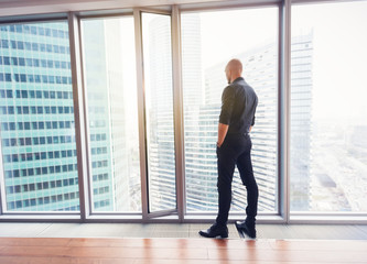 Fototapeta na wymiar Young attractive stylish bald man in a business suit in his office in a skyscraper, business, finance, success