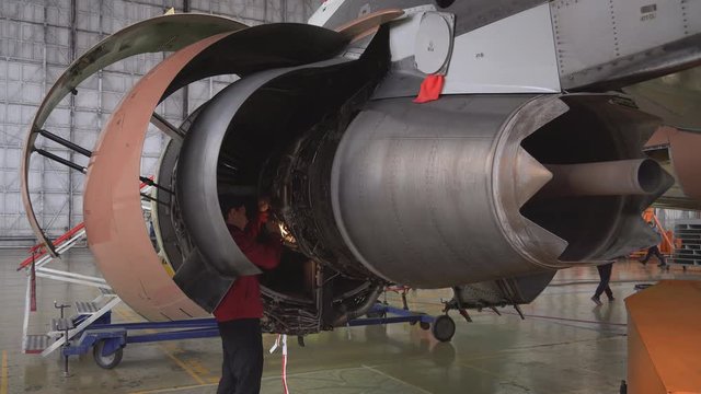 Engineer, technician examines the jet engine with a flashlight. The repair of aircraft in the hangar. Maintenance of aircraft. 4k