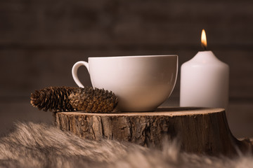 white cup with coffee, candle, cones and fur 