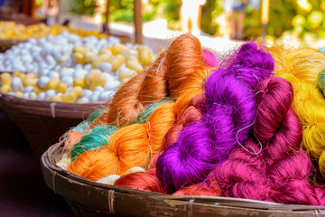 Colorful silk threads in wooden basket and blurred silk worm in background. Asian culture.