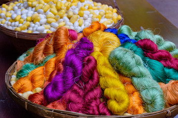 Colorful silk threads in wooden basket and blurred silk worm in background. Asian culture.