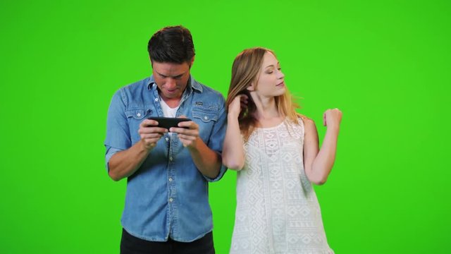 A man plays in his phone while his girlfriend/wife is trying to get his attention and succeeds, over a green screen.