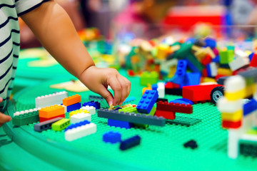 Close up baby child hand playing or creating the colorful plastic several size toy brick blocks in the tray.
