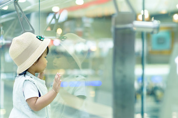 Asian cute girl child traveller feels lonely in the crowd at the mirror in department store or sidewalk at airport