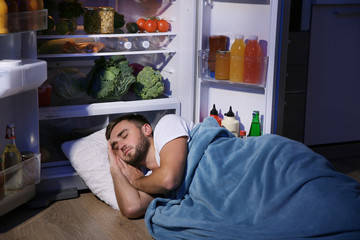 Young man sleeping near refrigerator at night
