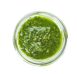 Homemade basil pesto sauce in glass jar on white background, top view