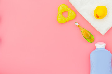 Baby care. Bath cosmetics and accessories for child with towel and yellow rubber duck on pink background top view copy space