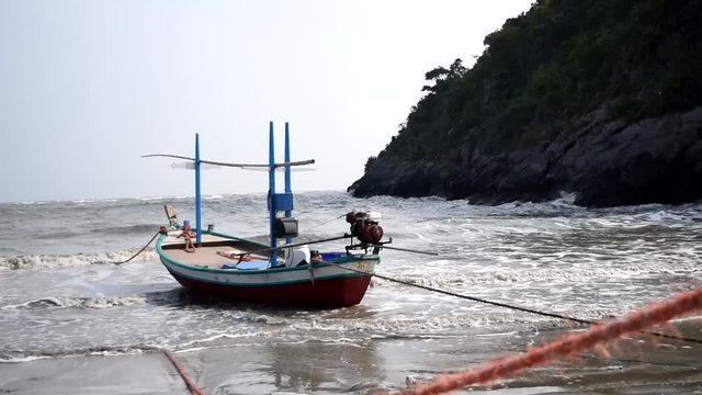 Fishing boat on the beach , Ocean waves splash the shore severely , Sea on the windy day , Bay with mountain  ,Thailand