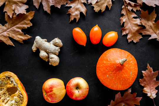Autumn garden harvest. Dried leaves, pumpkin, apple, tomatoes, ginger and nuts on black background top view