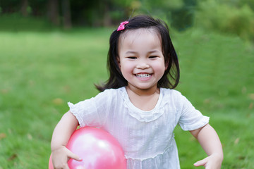 Asian happy smile cute little kid girl running in the public park or garden and holding rubber ball with her hand for play with parents.