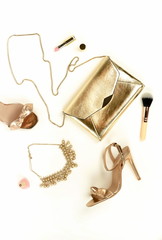 Flat lay, top view female high heels shoes sandals golden color, accessories clutch bag,  necklace and make up cosmetics on a white background. Glamour background.  Copy space .