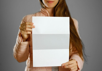 Naklejka premium A woman in a warm winter jacket holding a white leaflet. Blank paper. Close up. Isolated background